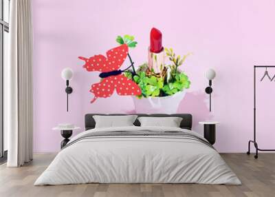 Lipstick in a pot with a green clover and a big red butterfly. Creative aesthetic nature inspired beauty and fashion layout against candy pink background.  Wall mural