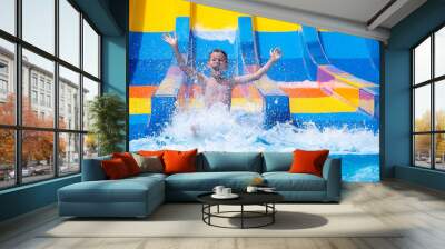 Cheerful boy splashing water on water slide at aqua park Wall mural