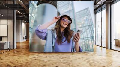 Excited young girl holding and using mobile phone Wall mural