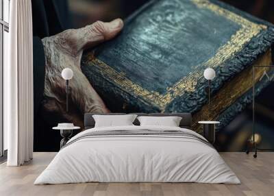 An elderly hand holds an ornate, antique book with gilded edges. Wall mural