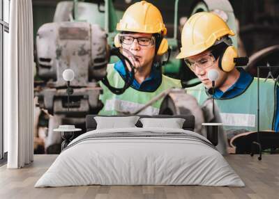 Work at factory.Two Asian workers man team working together in safety work wear with yellow helmet using Manual book.in factory workshop industry meeting professional Wall mural