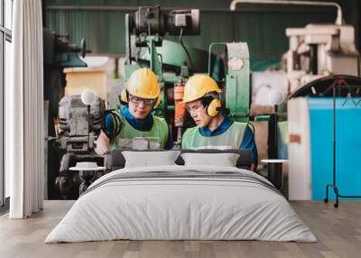 Work at factory.Two Asian workers man team working together in safety work wear with yellow helmet using Manual book.in factory workshop industry meeting professional Wall mural