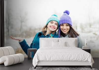 Two cheerful young women outdoors in winter laughing enjoying snowy day in park together Wall mural