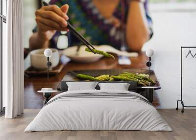 Woman eating grill asparagus with wooden chopsticks in restaurant. Wall mural