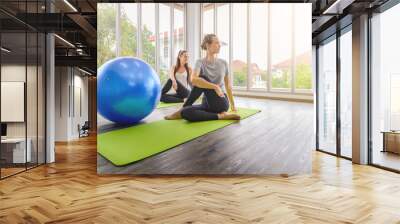 Two young beautiful women practicing yoga lesson on yoga mat, meditating in living room at home. healthy lifestyle concept Wall mural