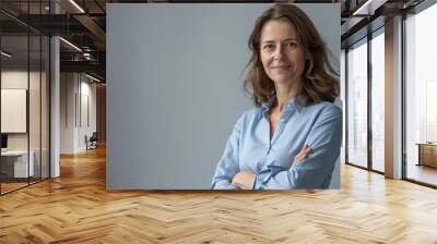 confident professional businesswoman in blue shirt with arms crossed smiling at camera gray background Wall mural