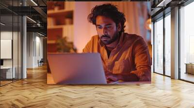 vibrant indian man engrossed in online webinar sitting at home with laptop warm lighting contemporary decor focused expression casual attire Wall mural