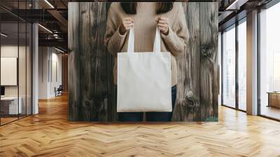 young woman holding blank white eco tote bag against rustic wooden background. minimalist mockup showcasing sustainable fashion and eco-friendly lifestyle choices. Wall mural