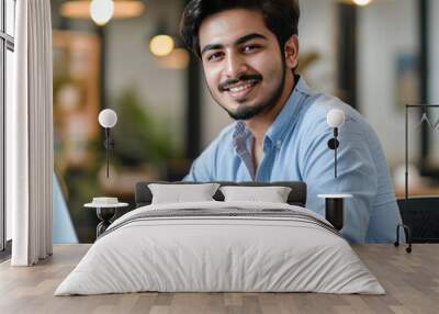 young handsome indian man using laptop and smiling Wall mural