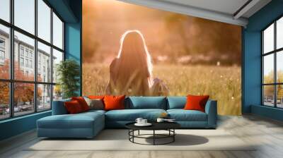 Back view of a woman with long hair sitting outdoors in sunlight enjoying nature. Wall mural