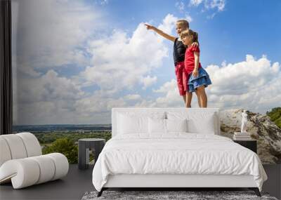 Little children boy and girl standing on mountain rock and looking ahead. Boy showing with his hand Wall mural