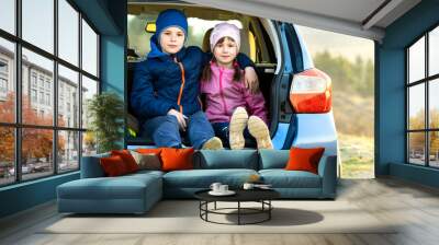 Two happy children boy and girl sitting together in a car trunk. Cheerful brother and sister hugging each other in family vehicle luggage compartment. Weekend travel and holidays concept. Wall mural