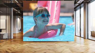 Young joyful child girl having fun swimming on inflatable air mattress in swimming pool with blue water on warm summer day on tropical vacations. Summertime activities concept Wall mural