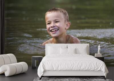 Young smiling child boy swimming in muddy water on sunny summer day. Active lifestyle and safety. Wall mural