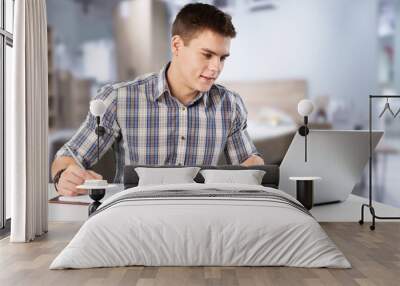 A happy young man works on his laptop with coffee at the table Wall mural