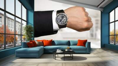 Businessman pointing at hand watch on grey wall background, close-up Wall mural