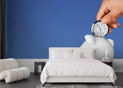 Hand depositing  clock  in piggy bank on background Wall mural