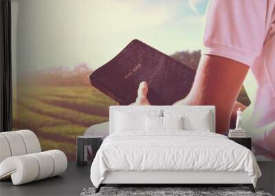 Human praying on the holy bible in a field during beautiful sunset. Wall mural