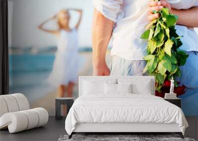 Man hiding bouquet of roses from woman at seaside Wall mural