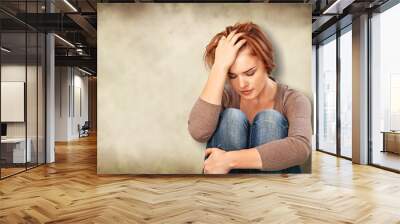 Worried woman sitting holding knees with arm on background Wall mural