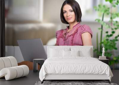 Young woman student using laptop in a video call or online class while sitting on sofa at home Wall mural