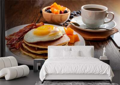 Delicious tasting breakfast of a stack of pancakes, two eggs, bacon, bowl of mixed fruit, and steaming coffee Wall mural