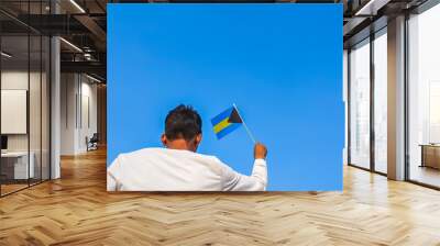 Boy holding Bahamas flag against clear blue sky. Man hand waving Bahamian flag view from back, copy space Wall mural