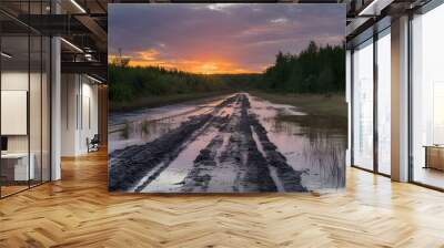 A dirt road with mud and grass. The road is partially submerged in water, with muddy water on one side and grass on the other. The road is surrounded by dense forest. Wall mural