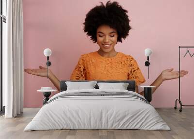 A young black African woman with open arms against a pink background. She has a beautiful afro-American hairstyle and a happy, smiling face, wearing a bright orange dress with a floral pattern.  Wall mural