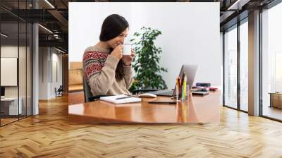 Young freelancer working from a makeshift home office connected to the internet with a laptop and a phone during the period of global confinement Wall mural