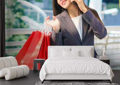 Beautiful shopper woman hand shopping with a smartphone and carrying red bag. concept of woker shopping and business online. Wall mural