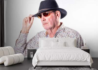 The image captures an elderly Caucasian man tipping his dark fedora hat with one hand. He wears sunglasses with a red tint, adding an air of mystery to his appearance. His attire includes a white Wall mural