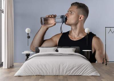 Athletic man drinking water against gray background Wall mural