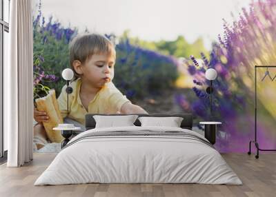 Cute hungry baby eating bread during picnic in a lavender field Wall mural