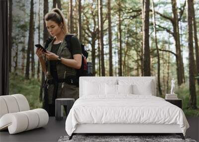 Female hiker is using smartphone for navigation in green forest Wall mural