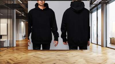 Front and back views of a man wearing a black, oversized hoodie with blank space, ideal for a mockup, set against gray background Wall mural