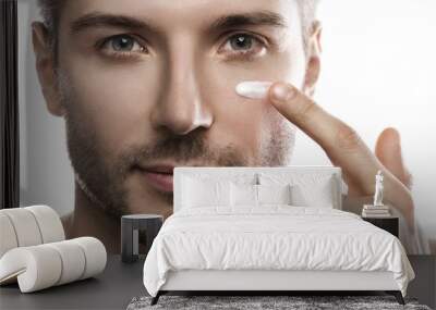 Men's beauty. Young man is applying moisturizing and anti aging cream on his face Wall mural