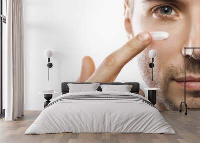 Men's beauty. Young man is applying moisturizing and anti aging cream on his face Wall mural