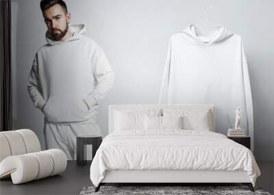 Mockup template. Man wearing white blank hoodie and other sample hanging nearby. Wall mural