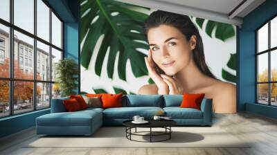 Portrait of young and beautiful woman with perfect smooth skin in tropical leaves Wall mural