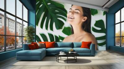 Portrait of young and beautiful woman with perfect smooth skin in tropical leaves Wall mural