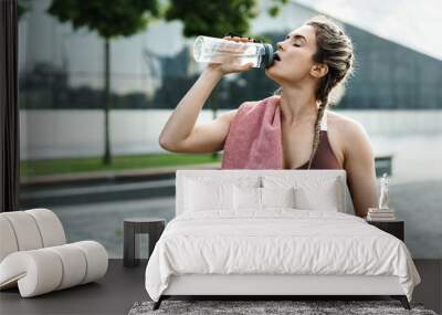 Tired woman drinking water after her fitness workout outdoors Wall mural