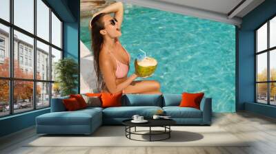 Woman relaxing in the swimming pool and drinking coconut water Wall mural