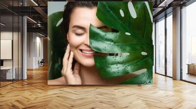 Young woman with a smooth skin holding Monstera deliciosa plant leaf Wall mural