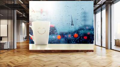 Happy Coffee Mug with smilely face on desk inside glass window, Blurred traffic jam light in city as outside view, Relaxing in cafe on rainy day Wall mural