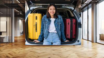 Smiling Asian young girl sit on suv car trunk with suitcases Wall mural