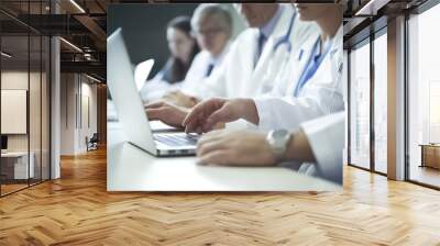 Medical team meeting in conference room. Medical team having a meeting with doctors in white lab coats and surgical scrubs seated at a table discussing and using computers in medical industry. 

 Wall mural