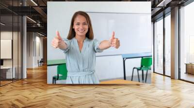 Happy female teacher with thumbs up in classroom. Wall mural