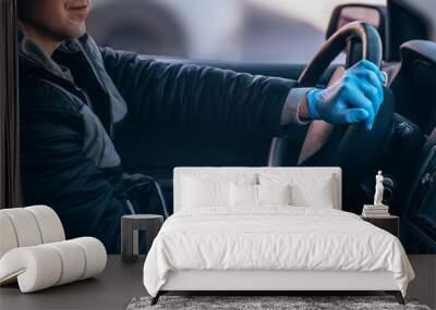 A man driving a car in a protective medical mask and gloves. Safe drive in a taxi during a pandemic coronavirus. Protect the driver and passengers from bacteria and virus infection in quarantine. Wall mural