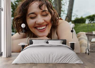 A cheerful young woman relaxes on a blanket, basking in the warmth of a sunny summer picnic. Wall mural